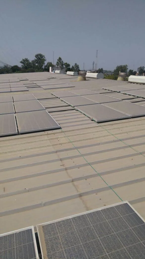 Heavily soiled rooftop solar PV installation showing uniformly dust-coated brownish module surfaces across multiple rows and array sections