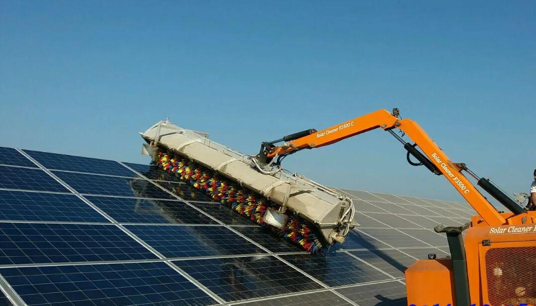 A vehicle-mounted rotating brush cleaning system in operation at a utility-scale ground-mounted solar PV plant, with the brush arm extended across module rows
