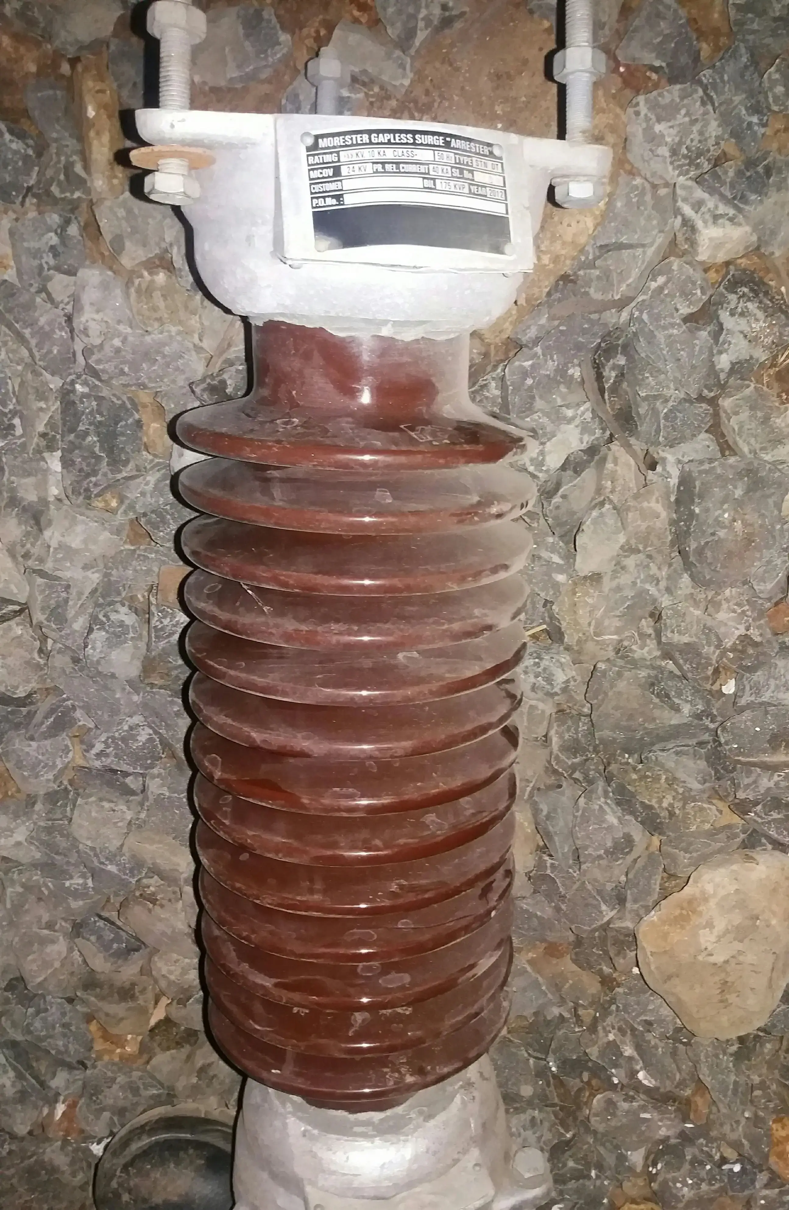 33 kV class porcelain disc-shed gapless surge arrester with metal top and bottom caps installed at a utility-scale solar plant HV substation yard, eleven porcelain disc sheds visible, earthing conductor exits from bottom cap