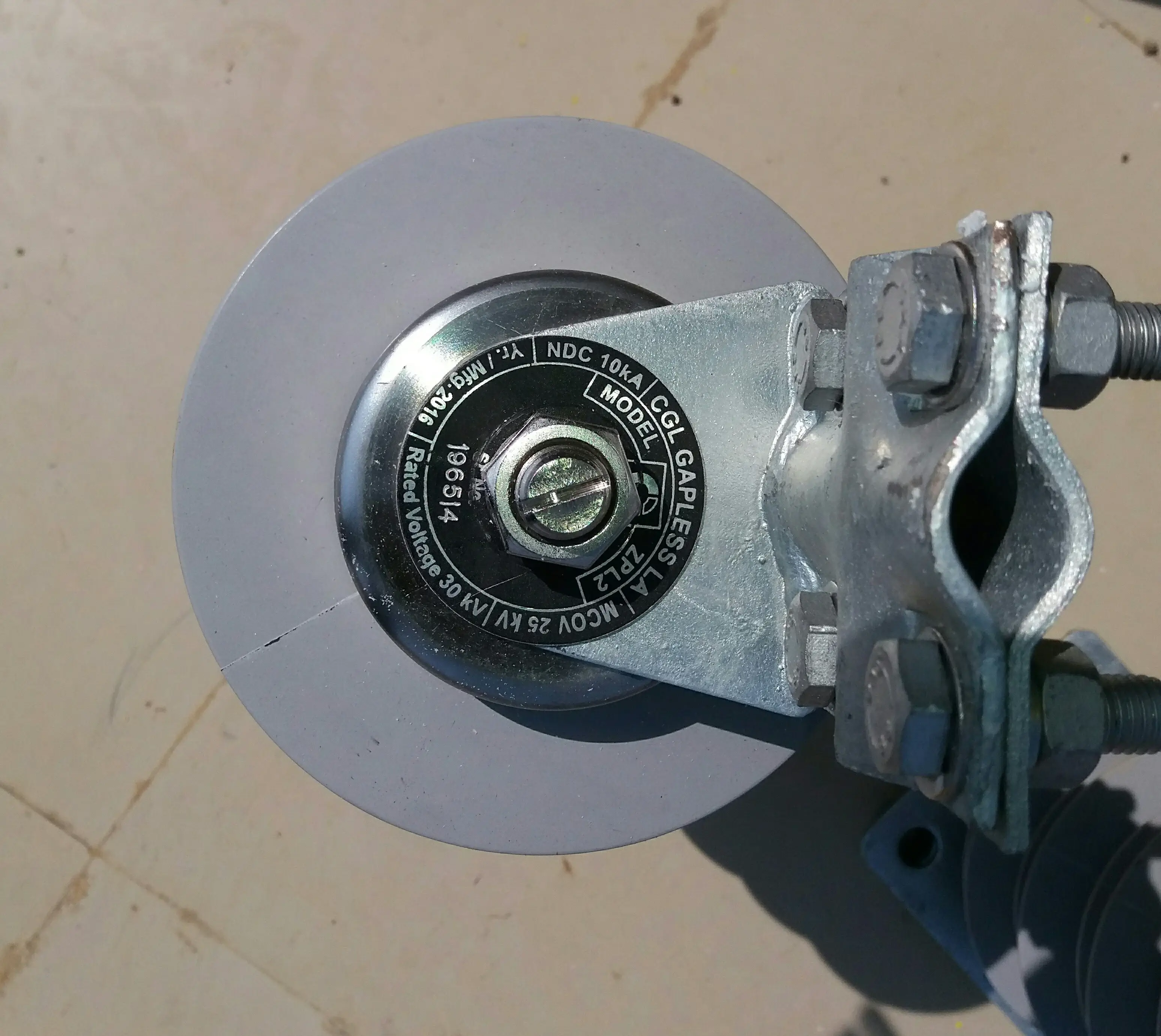 Close-up of gapless lightning arrester model ZPL2 bottom cap nameplate showing NDC 10kA, MCOV 25kV, rated voltage 30kV, with ground clamp hardware visible