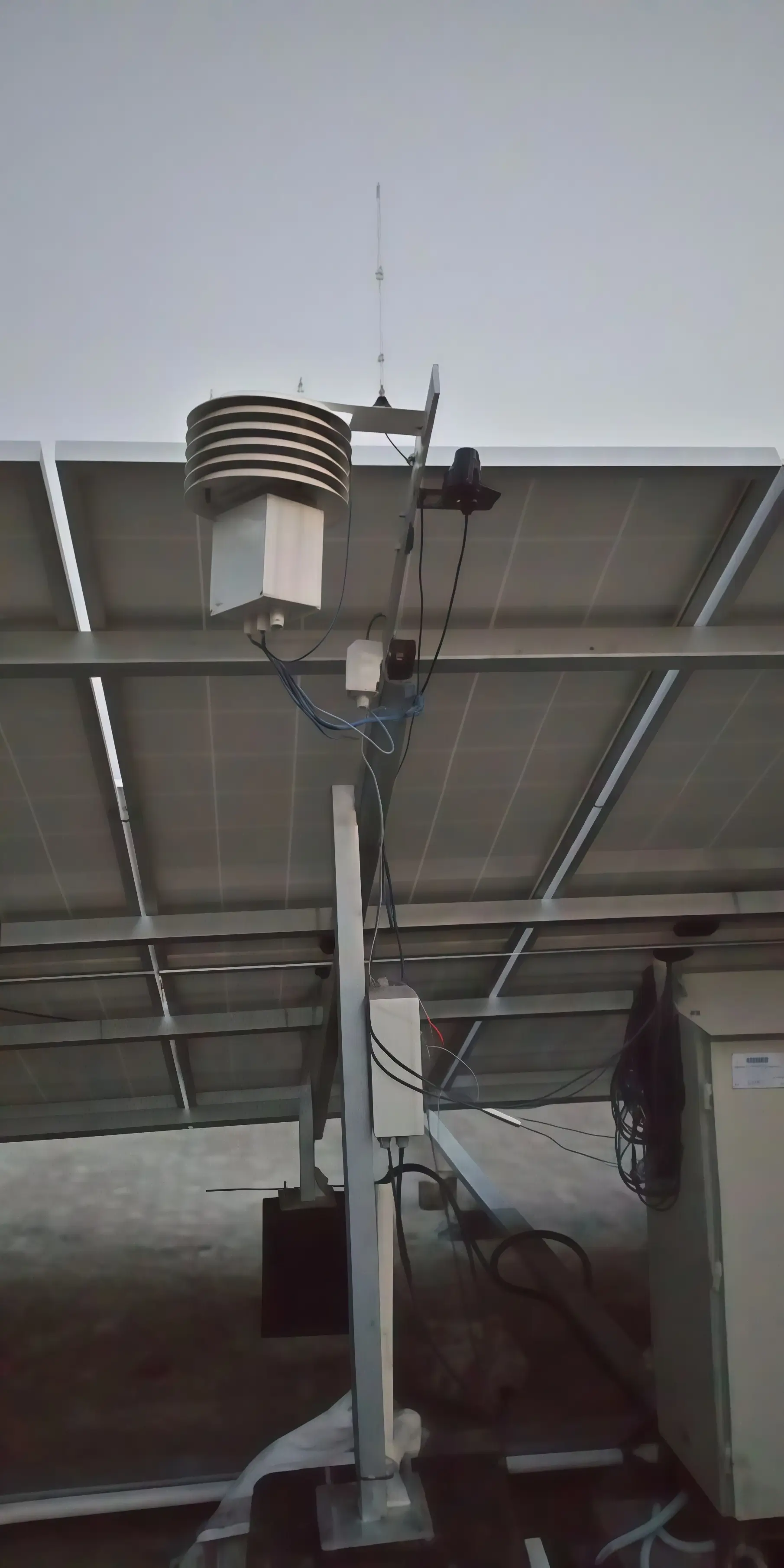 Weather monitoring station with radiation-shielded temperature sensor and pyranometer mounted on a utility-scale solar PV plant structure for POA and GHI irradiance measurement