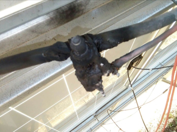 Severely burned and charred solar PV insulation piercing connector and junction box on a panel frame, showing the result of high contact resistance and thermal runaway in a DC cable connection