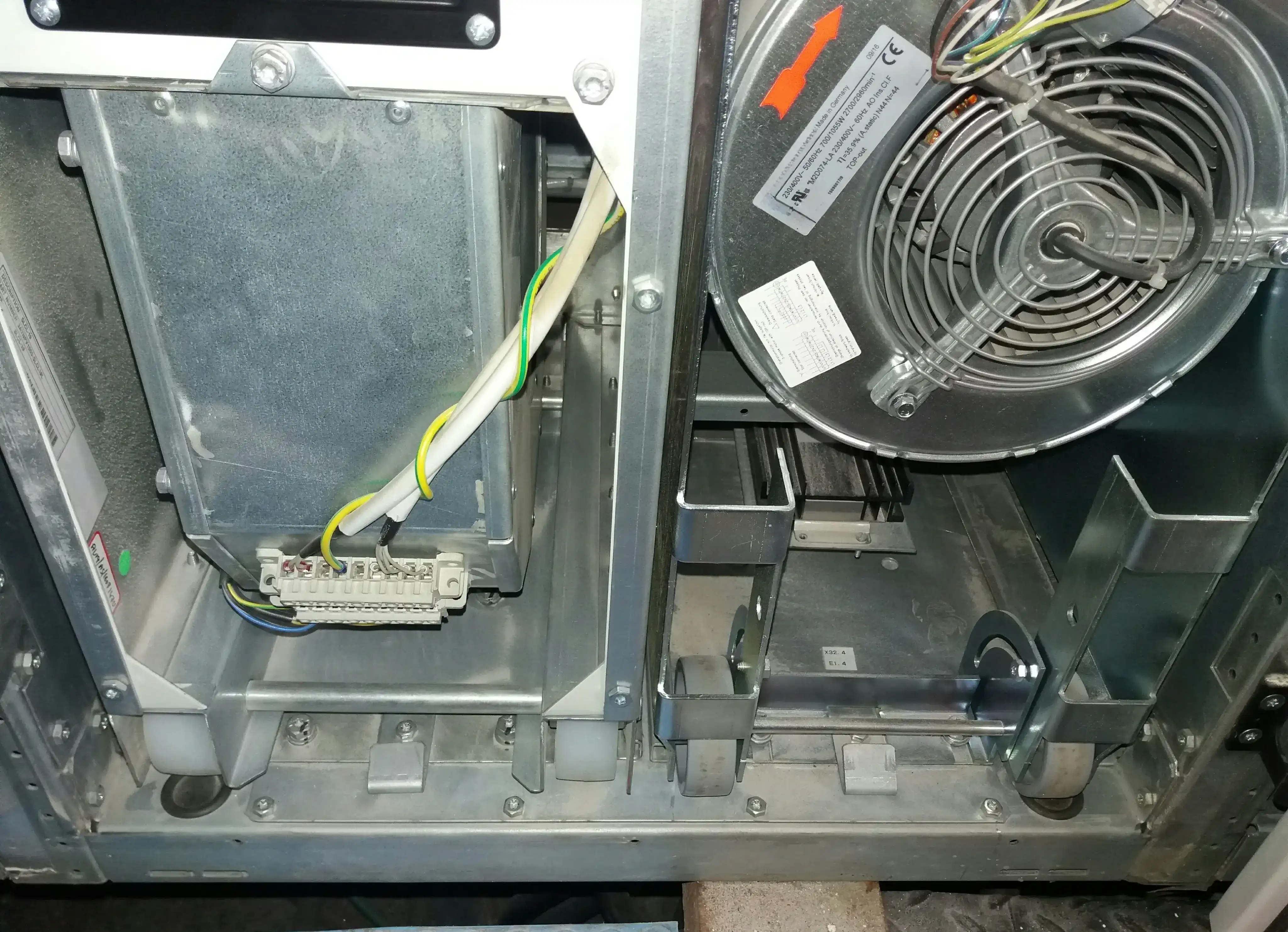 Interior of utility-scale central solar inverter showing two adjacent cooling fan bays during fan replacement: left bay empty after failed fan removal with terminal block wiring exposed, right bay with replacement centrifugal blower fan installed