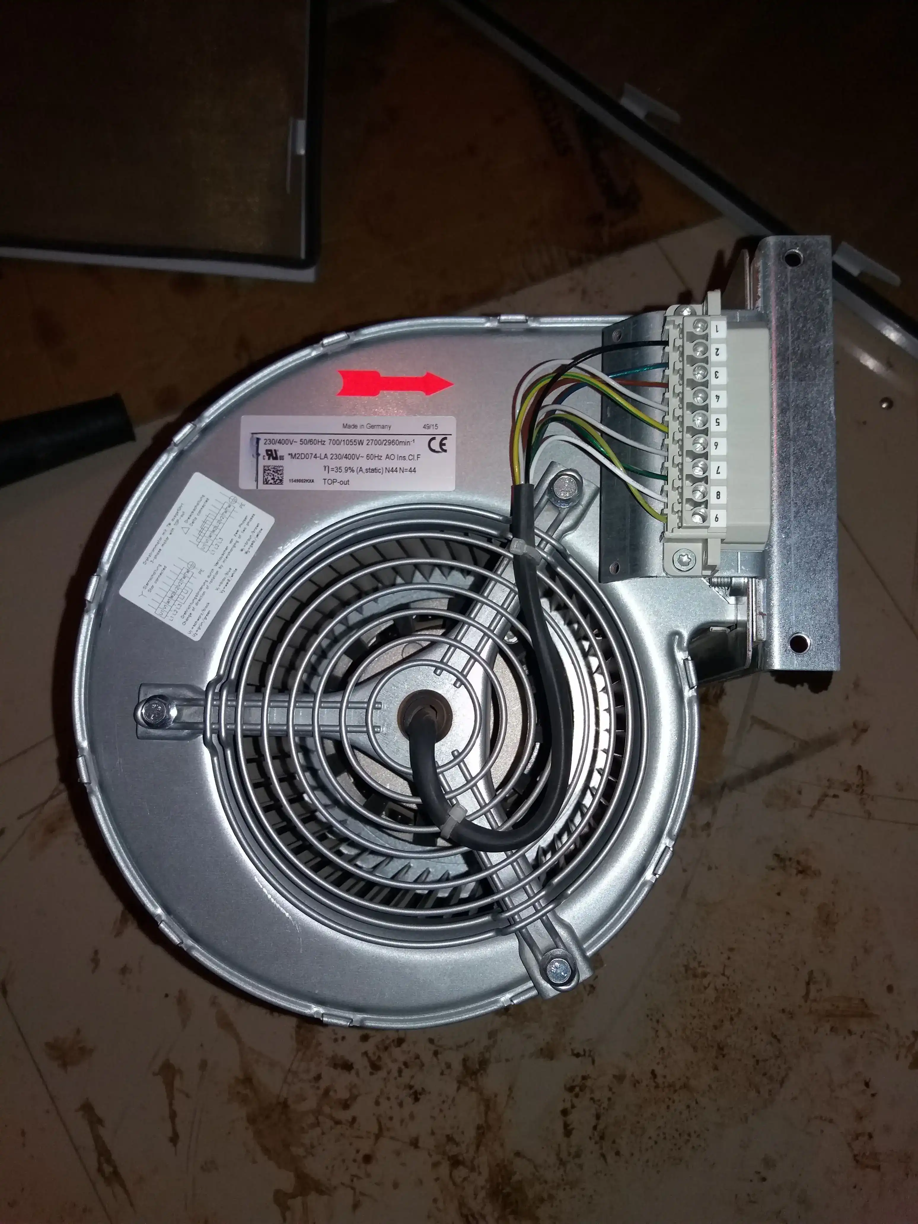 Replacement centrifugal blower fan for a utility-scale central solar inverter, nameplate showing 230 400V 50 60Hz 700 1055W 2700 2960 rpm, with multi-pin terminal block connector, placed on plant floor before installation