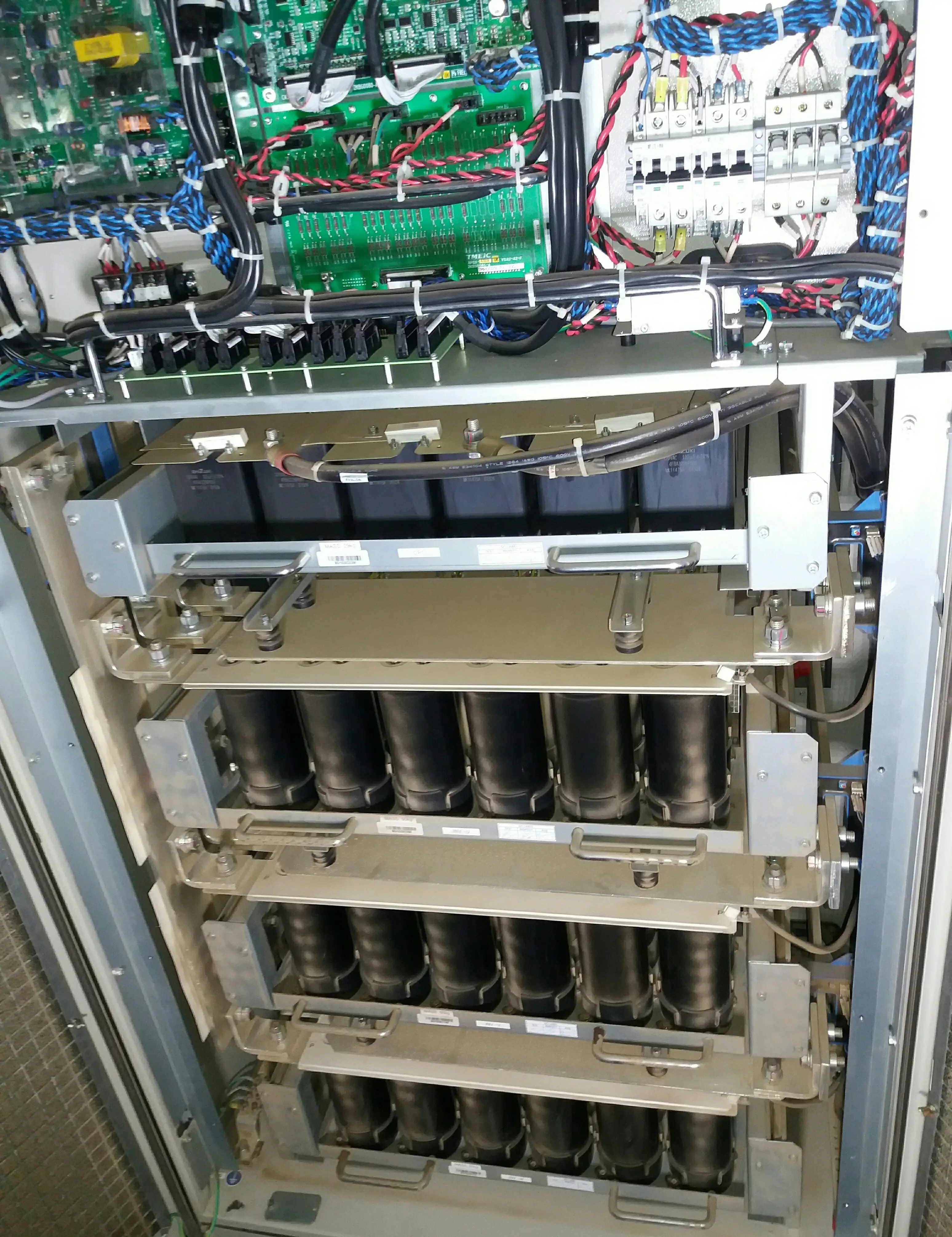 Interior of a central inverter at a utility-scale solar plant showing four rows of large black DC link electrolytic capacitor banks and a green control PCB at the top