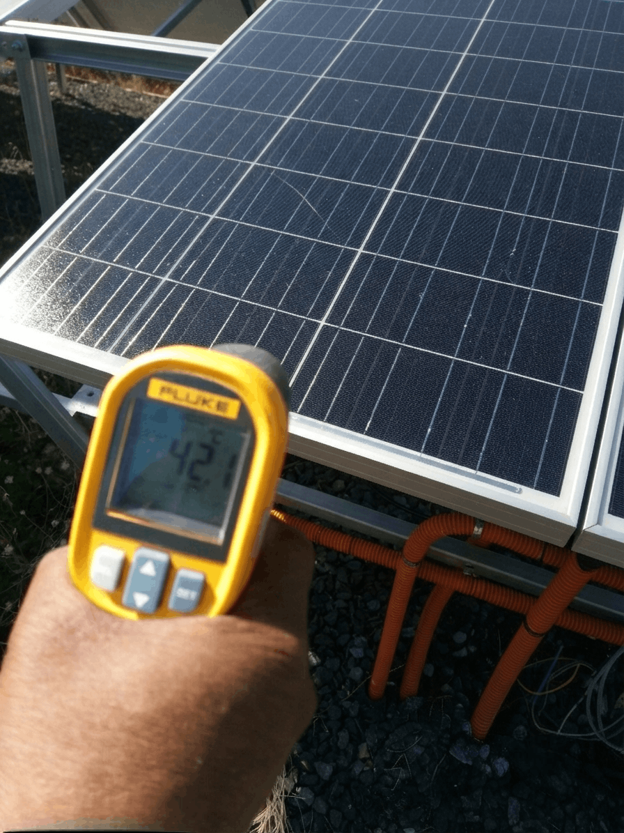 Fluke infrared thermometer reading 42°C on the front glass surface of a polycrystalline solar panel mounted on a ground-mount racking structure