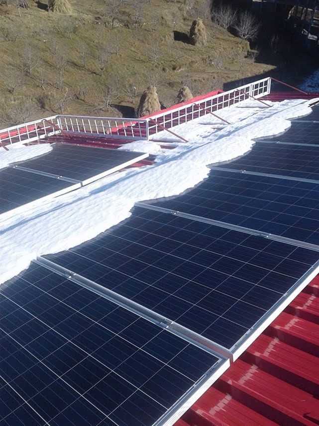 Partial snow coverage on rooftop solar PV modules at a high-altitude installation, showing uneven melt pattern with some modules fully clear and others partially snow-covered, December 2017