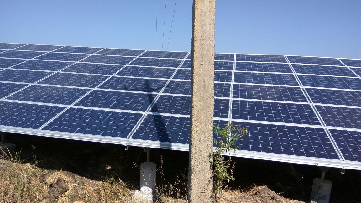 A concrete utility pole casting a diagonal shadow across multiple solar PV modules in a ground-mounted array, photographed on 11 November 2016